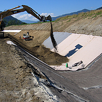 Cubrimiento del canal de agua mediante la instalación de esteras de hormigón y posterior relleno de arena con ayuda de una excavadora.