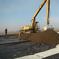 Excavadora trabajando, esparciendo tierra sobre el tejido de refuerzo Basetrac® Woven colocado