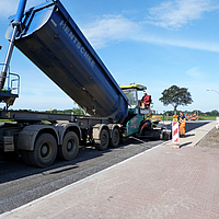 Camión volquete vierte asfalto en una máquina de término para asfaltar una carretera con material compuesto SamiGrid