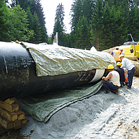 Los trabajadores fijan la cubierta de tuberías Incomat® al tramo de tubería