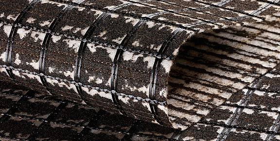 Refuerzo de asfalto SamiGrid® - vista de cerca del material  Primer plano del compuesto SamiGrid® de rejilla de PVA y tejido no tejido saturado de betún